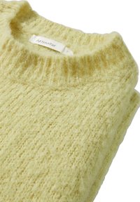 Pull en tricot jaune avec un col rond côtelé, texture douce et motifs de couture visibles ; l'étiquette indique "hessnatur."