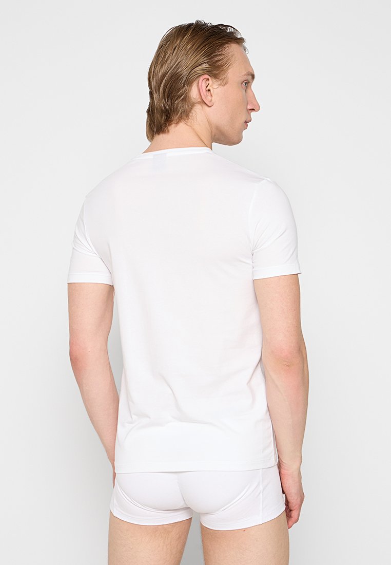 Weißes, enges, kurzärmliges T-Shirt mit glatter Textur, Rundhalsausschnitt, kombiniert mit weißer Unterwäsche, von hinten vor einem schlichten Hintergrund zu sehen.