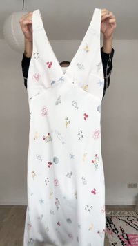White sleeveless dress with deep V-neck, decorated with small colorful sea-themed and floral prints, held up by a person.
