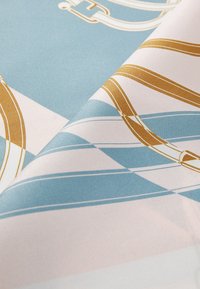 Silkkihuivi, jossa on vaaleansininen ja valkoinen geometrinen kuvio, kultaisilla yksityiskohdilla. Sujuva pinta, taiteltu näyttämään yksityiskohtia ja muotoilua.