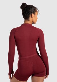 Burgunderfarvet atletisk top med lange ærmer og rund hals, der har ribbet tekstur og en tætsiddende design. Parret med matchende tætsiddende shorts.