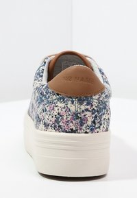 Sneakers med ett texturerat tyg som har ett flerfärgat prickigt mönster, beige läderhælaccent och en vit gummisula.