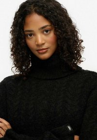 Czarny sweter z golfem wykonany z puszystego materiału o teksturowanym wzorze dzianiny. Charakteryzuje się obniżonymi ramionami i małą metką na rękawie.