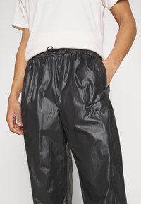 Zwarte, glanzende windbreakerbroek met elastische tailleband en zijzakken. Voorzien van een klein zwart Nike Air-logo op het linkerbeen. Lichtgewicht materiaal.