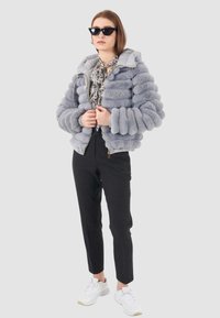 Giubbotto a bolla grigio con tessuto texturizzato e arrotondato, con chiusura a zip e cappuccio. Abbinato a pantaloni a righe nere e sneakers bianche.