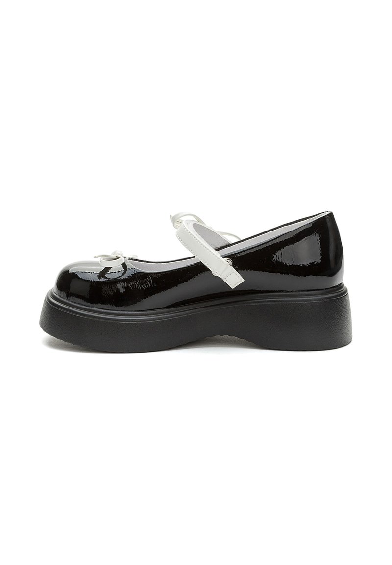 Scarpe Mary Jane in vernice nera con cinturino bianco e dettaglio a fiocco. Presenta una spessa suola piattaforma nera. Vista laterale.