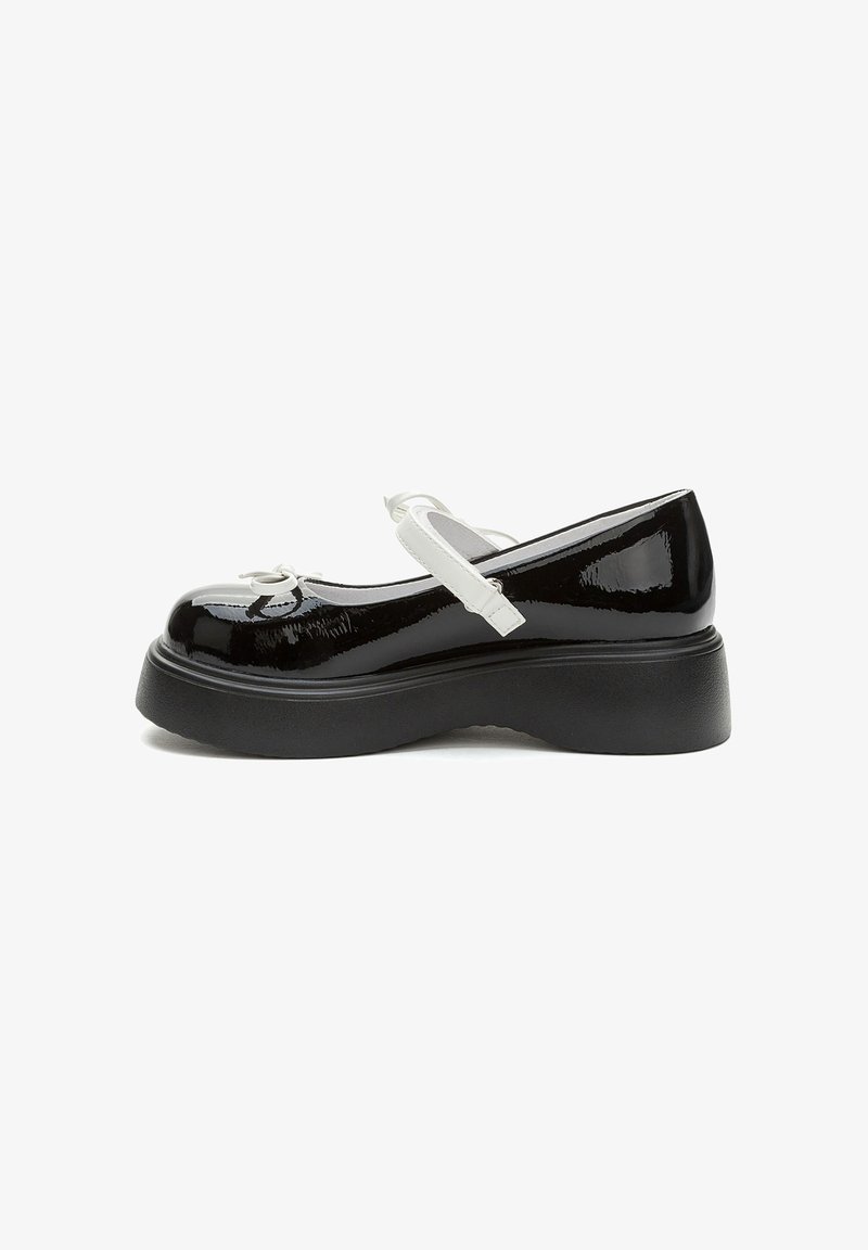 Scarpe Mary Jane in vernice nera con cinturino bianco e dettaglio a fiocco. Presenta una spessa suola piattaforma nera. Vista laterale.