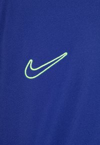 Tejido morado de Nike con un logotipo de swoosh bordado en verde neón, textura suave y un diseño atlético simple.