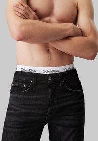 Jean en denim noir avec une ceinture logo Calvin Klein blanche. Comprend cinq poches, un matériel en métal et une coupe slim.