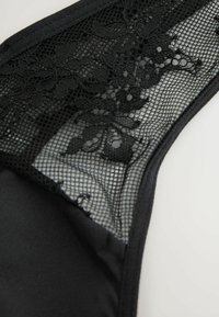 Zwarte kanten string met een mesh bloemmotief, een gladde satijnen stof, elastische tailleband en contrasterende texturen.