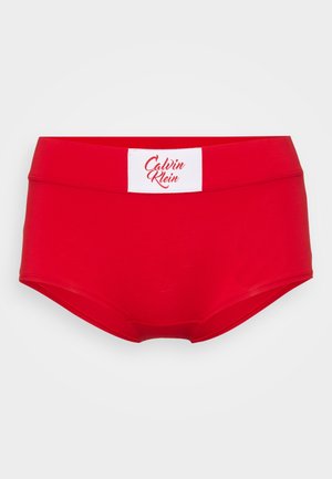 Rode katoenen slips met een brede tailleband, voorzien van een witte label met de tekst "Calvin Klein" in sierlijke letters. Klassieke silhouet en een gladde textuur.