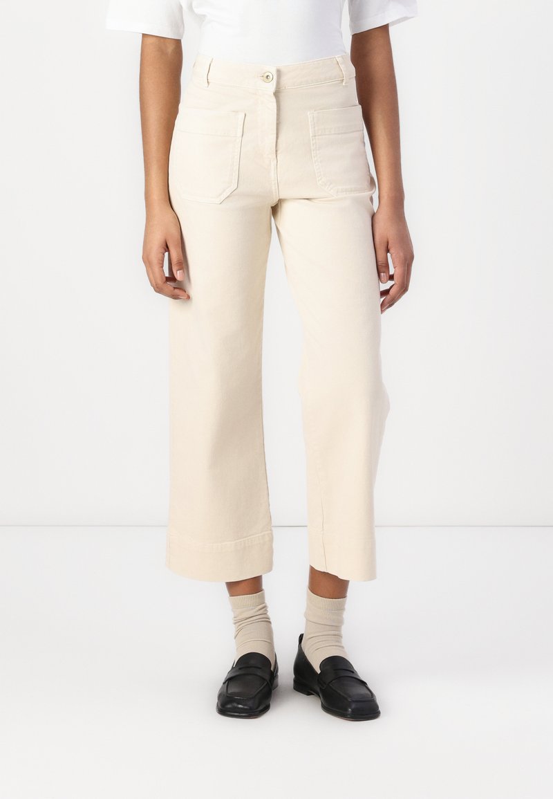Pantaloni a gamba larga in cotone beige chiaro, con vita alta, chiusura frontale con bottone e due tasche posteriori. Accentuati da un orlo pulito.