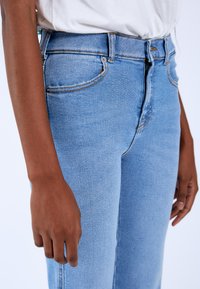Jeans de mezclilla azul claro de cintura alta, con bolsillos cosidos y cierre de cremallera. La tela tiene una textura suave y un ligero estiramiento.