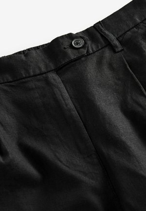 Black linen trousers with a button closure and elastic waistband. The fabric appears textured with visible stitching details.