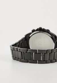 Montre en acier inoxydable noir avec un bracelet à maillons épais, présentant un boîtier rond et une finition polie des deux côtés.