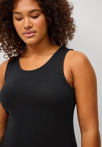Top negro sin mangas hecho de un tejido suave, con un escote redondeado y una silueta ajustada que resalta la parte superior del cuerpo de quien lo lleva puesto.