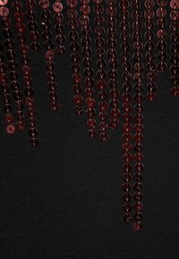 Black fabric adorned with red sequin embellishments, cascading vertically in a pattern, creating a textured, shimmering effect.