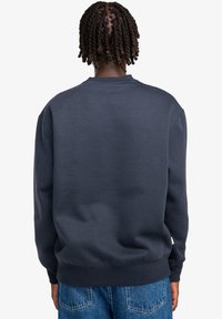 Felpa girocollo di un blu navy scuro con polsini e orlo a costine. Tessuto solido senza motivi visibili, abbinata a jeans a vita alta di un blu chiaro.
