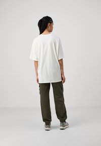 Hvid oversized t-shirt med korte ærmer, parret med olivengrønne cargo-bukser. Casual stil og en afslappet pasform, vist fra bagsiden.