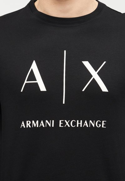 Черна тениска с бели букви "A | X" и текст "Armani Exchange" отпред на гърдите.