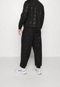 Černý sportovní komplet s raženými logy "ADIDAS", volného střihu, s žebrovanými manžetami, doplněný o bílé sportovní boty.