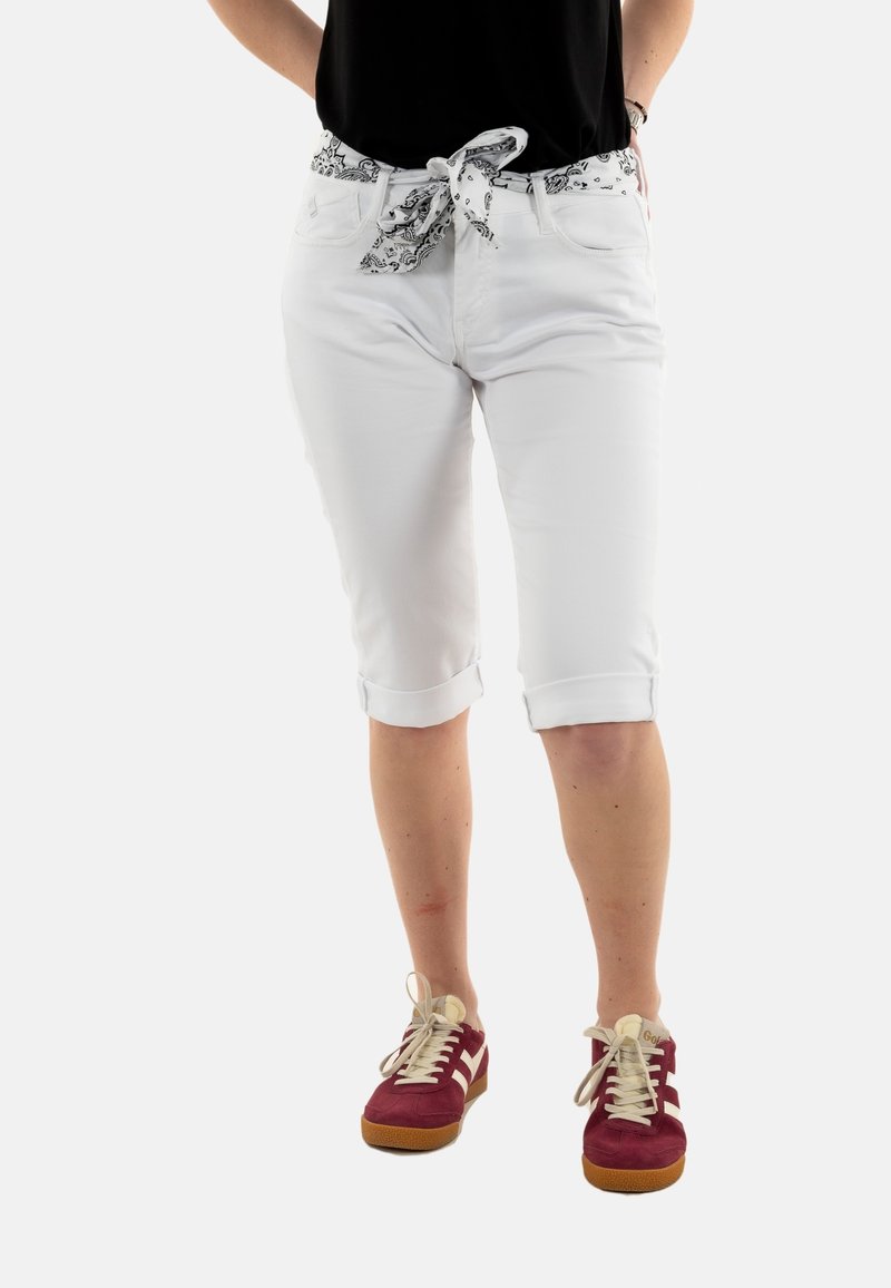 Witte knielange broeken met een zwart-wit gestreepte riem, opgerolde pijpen en voorzakken, gedragen met rood-witte sneakers.