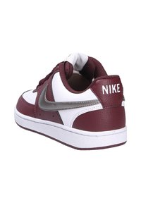 Baskets Nike avec un haut en cuir bordeaux, accents blancs, swoosh argenté, col rembourré et semelle en caoutchouc texturé.