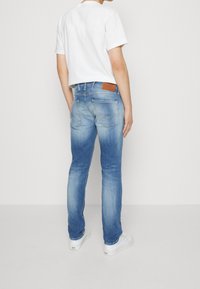 Blekta blå denimjeans med rak passform, som har en brun läderpatch på bakre midjan och subtila sömmar på fickorna.