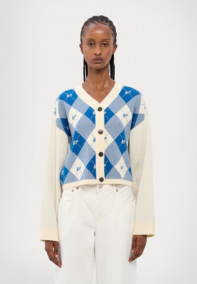 Cardigan bleu et blanc à motif argyle avec de longues manches crème, devant boutonné et col côtelé. Tissu tricoté avec des accents graphiques.