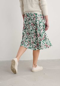 Floral print skirt in green, featuring pink and white flowers. A-line shape, mid-length, made of lightweight material, paired with beige sneakers.