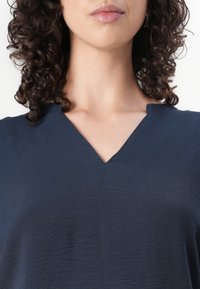 Navyblaues Oberteil mit V-Ausschnitt-Design, weichem Griff und subtiler Schimmer, akzentuiert mit kurzen Ärmeln und einem lockeren Schnitt.