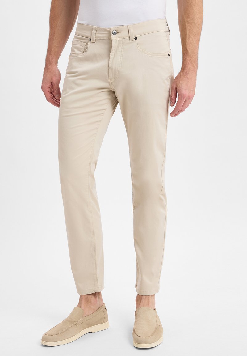 Beige Baumwollmischungshose mit schlanker Passform, mit Seitentaschen und einer glatten Textur. Kombiniert mit hellen Slippers.