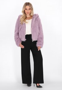 Giacca cappotto effetto pelliccia lilla con cappuccio, zip frontale, polsini a coste e una texture morbida, abbinata a pantaloni neri a vita alta a gamba larga.