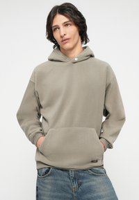 Hettegenser i lys grå fleece med kengurulomme, ribbede mansjetter og trykknappdetalj. Uformell design.