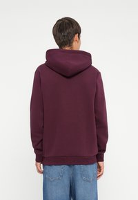 Bordeaux hoodie met een trekkoordkap, ribbelmanchetten en zoom. Zachte textuur, relaxte pasvorm en gladde naden. Gecombineerd met lichte spijkerbroek.