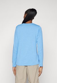 Long-sleeve shirt in light blue fabric. Soft texture with a round neck, relaxed fit, and straight hem. Worn with light beige pants.