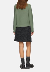 Grüner gerippter Pullover, schwarzer gesprenkelter Rock und schwarze Stiefeletten mit grauen Sockenakzenten, von hinten betrachtet. Schlichtes, strukturiertes Design.