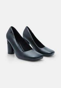 Pump nere in pelle con tacco alto, punta quadrata, superficie liscia e tacco spesso e lucido. Dettaglio logo discreto vicino al tacco.