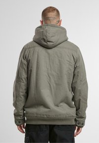 Chaqueta verde oliva con capucha, con cierre de cremallera en la parte delantera, puños de canalé y bolsillos laterales. Acabada con tela texturizada y costuras visibles.
