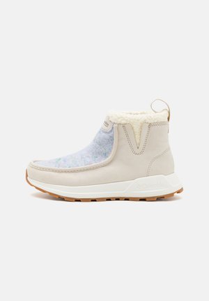 Beige slip-on støvel med grå filtemiddel, hvit fleecekrage og brun gummisåle. Har en trekkflik bak for enkel påkledning.