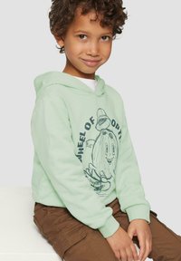 Mintgroene sweatshirt met een capuchon, voorzien van een grafische print op de voorkant en ribgebreide mouwen. Bruine broek met cargopockets.