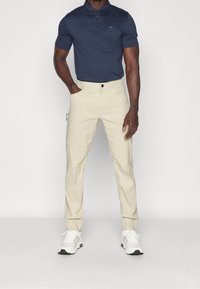 Marinblå pikétröja med knappslå och logotyp, kombinerad med beige chinos och vita sneakers med svarta accenter. Slitstukt tyg och skräddarsydd passform.