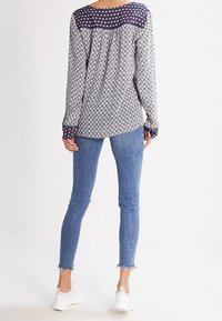 Blusa a maniche lunghe con yoke mio blu a motivo e stampa geometrica bianca. Abbinata a jeans skinny azzurri e sneakers bianche.
