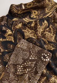 Long-sleeve turtleneck top in a ribbed fabric featuring a brown and gold abstract pattern, with dark blue accents and a textured finish.