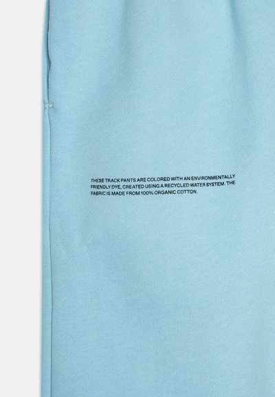 Pantalones de chándal azul claro hechos de 100% algodón orgánico, con una textura suave y una pequeña etiqueta impresa con instrucciones de cuidado.