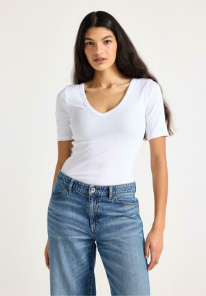 Vit kortärmad V-ringad topp med ribbad textur, kombinerad med ljusblå högmidjade jeans med klassisk femfickdesign.