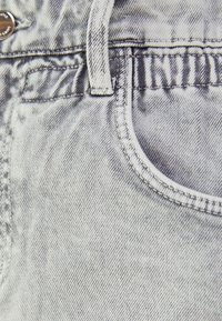 Tela de mezclilla gris claro que muestra un primer plano de la costura del bolsillo, superficie texturizada y detalles de la cinturilla con un botón metálico.