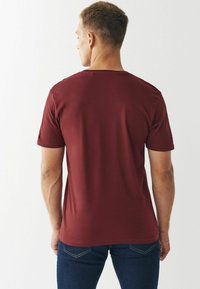 Morris kortærmet t-shirt i bordeaux lavet af bomuldsblanding. Rund halsudskæring, glat tekstur og tætsiddende snit. Bæres med mørkeblå jeans.