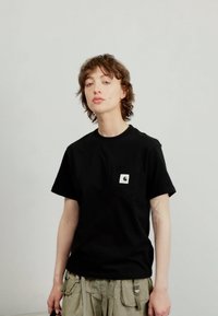 T-shirt noir à manches courtes avec un col rond et une poche à l'avant. Présente un patch logo sur la poche. Le tissu semble doux et lisse.