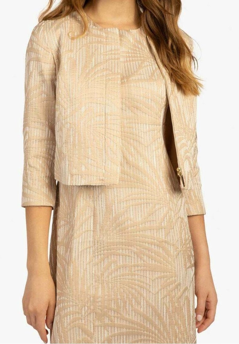 Robe beige texturée accompagnée d'une veste courte, présentant un motif ondulé, des manches trois-quarts et une fermeture éclair latérale sur la veste.